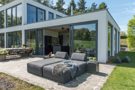 Terrasse mit gemütlichen Sitzmöbeln und einer geöffneten Hebeschiebtür und Holz-Alu-Fenstern der Fusionline von Gaulhofer.