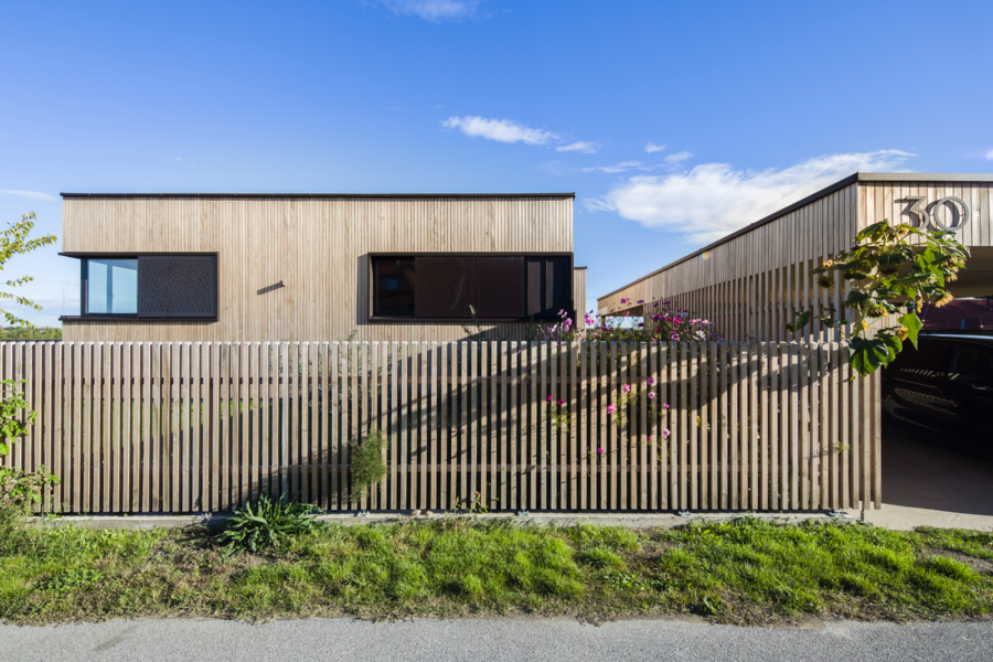 Einfamilienhaus mit Flachdach, Holzfassade, passendem Gartenzaun und Eckfenstern von Josko.