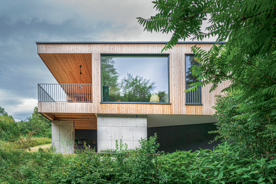 Hanggebautes Holzriegelhaus mit Flachdach, Balkon und bodentiefer Verglasung von Weissenseer Holz-System-Bau.