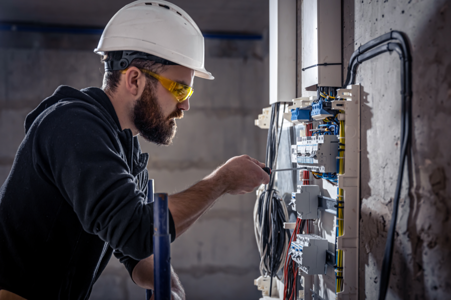 Elektriker arbeitet in einer Schalttafel mit einem Schraubenzieher an einem elektrischen Verbindungskabel und führt Elektroinstallationen aus.