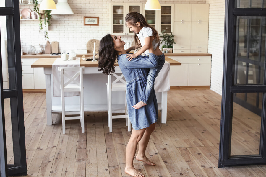 Junge Mutter hebt Ihre kleine Tochter voller Freunde in der modern eingerichteten Altbauwohnung mit hohen Räumen und breiten Durchgangstüren in die Höhe und hat Spaß.