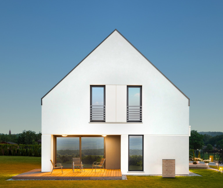 Wärmepumpen-Außeneinheit mit holzverkleideter Front und indirekter Beleuchtung vor einem modernen Wohnhaus von Dimplex.