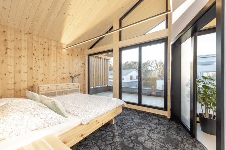 Erler Haus zeigt ein sehr helles Schlafzimmer mit hohen Decken, schwarzen Türrahmen, Balkon  und dunklen Boden.