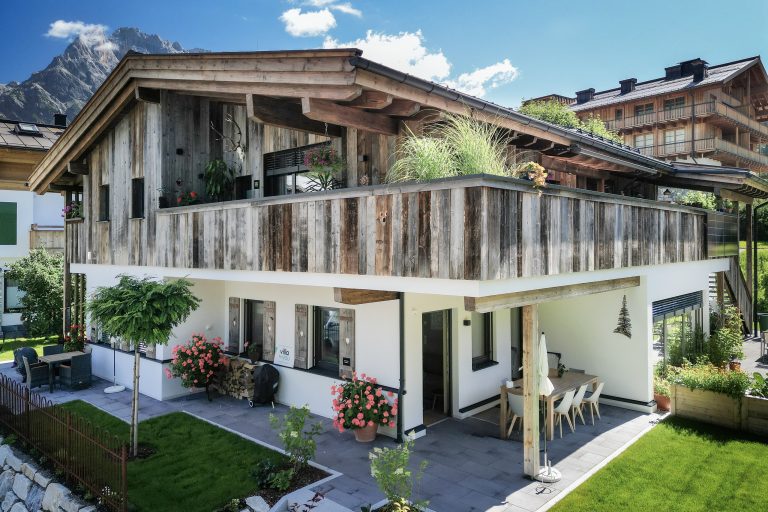 Erler Haus zeigt Einfamilienhaus mit Satteldach, rustikaler Holzfassade, Balkon mit Holzgeländer und Terrasse.