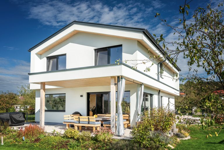 Erler Haus zeigt Einfamilienhaus mit Satteldach, weißer Fassade, überdachter Terrasse und Garten.