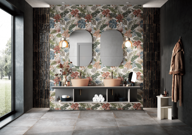 Fliesendorf zeigt ein Badezimmer mit rosa Doppelwaschbecken, zwei ovalen Spiegeln auf der Wand mit Wandfliesen im Blumenmuster und Bodenfliesen im Metall-Look.