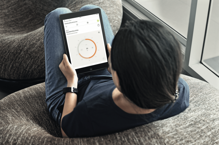 Gira zeigt einen jungen Mann auf einem dunklen Sitzsack mit schwarzem iPad und der App zur Steuerung der Lichteinstellungen für das Smarthome.