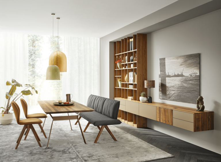 WOHNHAUS Grill & Ronacher zeigt eine moderne Essgruppe von ANREI, bestehend aus einem Esstisch aus dem Holz der Astnuss sowie Sideboards aus dem Holz der Astnuss sowie Stühle und Sitzbank mit Stoffbezug sowie dazupassendem Wandboard mit anbauregal..