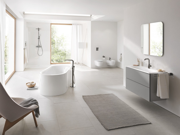 Badezimmer mit freistehender Wanne, einem Essence Keramik Waschtisch, dem Euphoria Smart Control Duschsystem, der Betätigungsplatte Arena Cosmopolitian und Essentials Accessoires von Grohe.