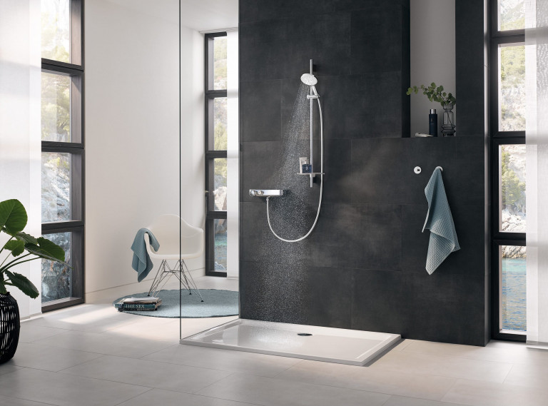 Duschnische mit silber Chrom-Armaturen von Grohe, Glastrennwand und dunklen Wandfliesen.