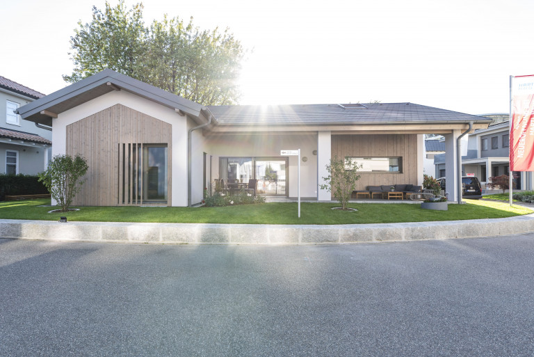 Bungalow mit Satteldach, holzverkleideten Fassaden, überdachter Terrasse mit Stützsäulen von Hartl Haus.