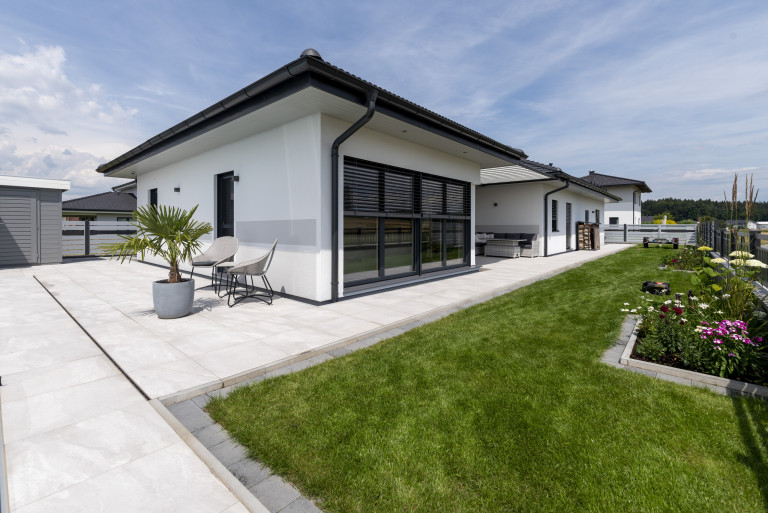 Bungalow mit Satteldach, Terrasse mit hellem Steinboden und Loungebereich zwischen den Gebäuden von Hartl Haus.