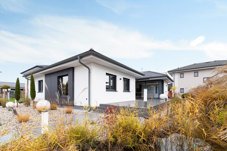 Ein Bungalow von Hartl Haus mit Satteldach und weissem Rauputz mit einem Fassadenelement in Anthrazit im Musterhauspark.