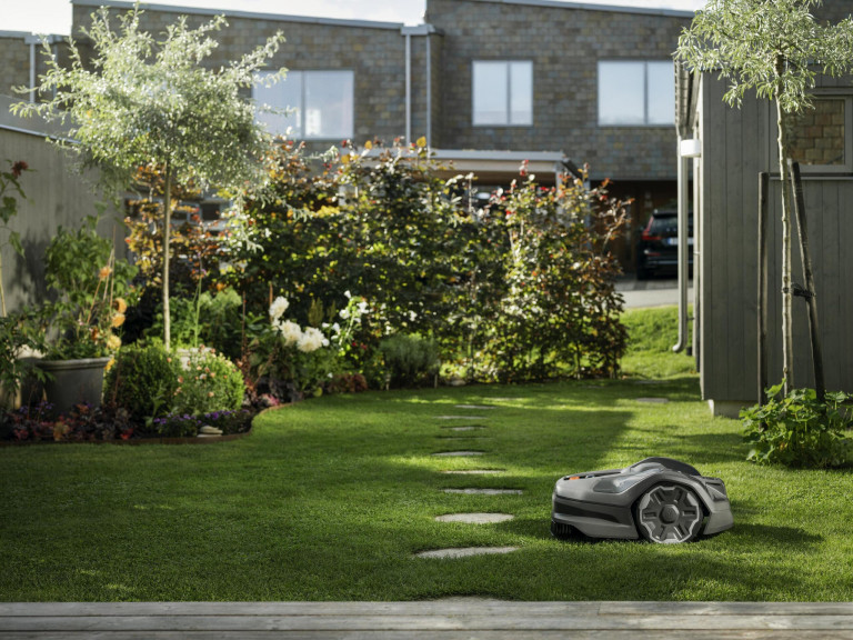 Ein kabelloser Mähroboter mäht den Garten hinter dem Haus von Husqvarna.