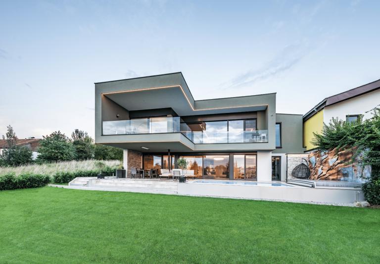 Modernes Flachdach-Wohnhaus mit Glasgeländer Balkon, großer Terrasse mit Pool und Stiegenabgang in den Garten und vielen raumhohen Fenstern und Glasschiebetüren von Internorm.