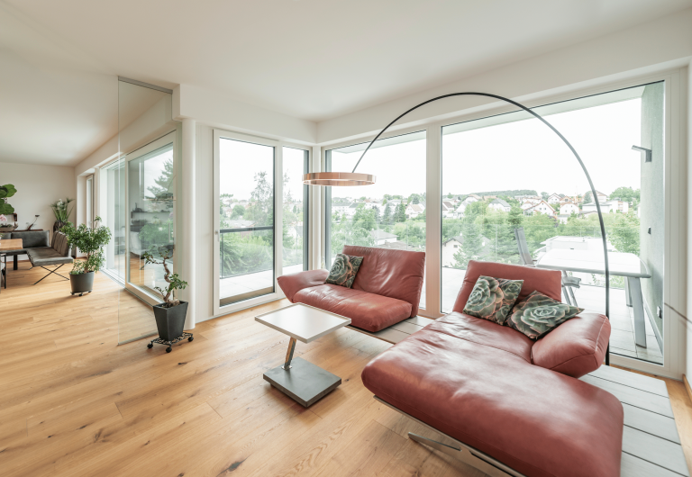 Helles Wohnzimmer mit Holzboden und großen Fensterfront mit Glasschiebetür und Glastür von Internorm, die auf den Balken führen.