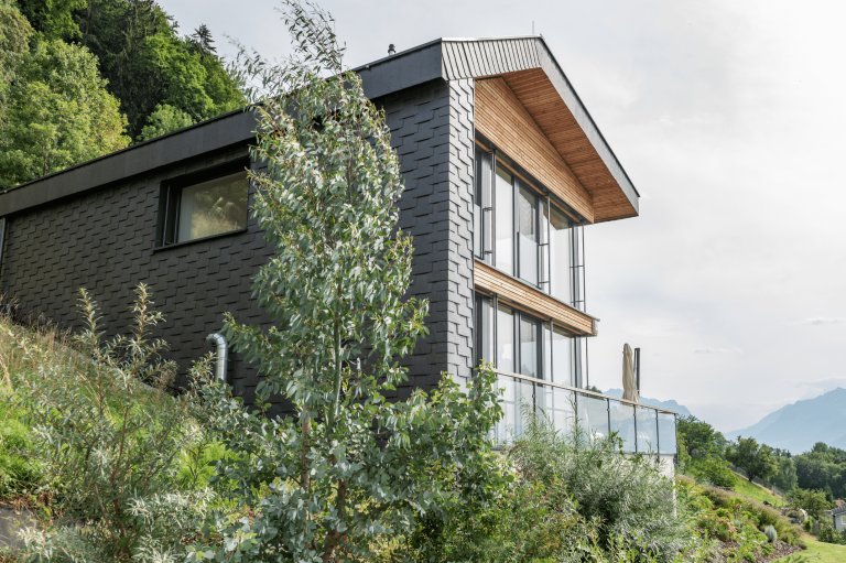 Internorm zeigt ein schwarzes Einfamilienhaus mit Holzakzenten, vielen Glasfronten und einen Balkon mit Glaswand und Metallgeländer.