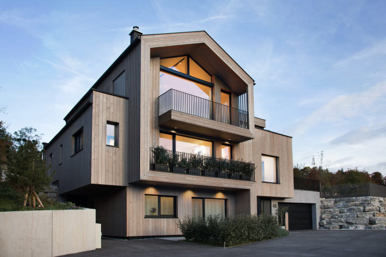 Modernes zweistöckiges Holzhaus mit zwei Balkonen, großen Glasfronten, Glasschiebetüre und Giebelfenstern mit schwarzem Rahmen von Josko.