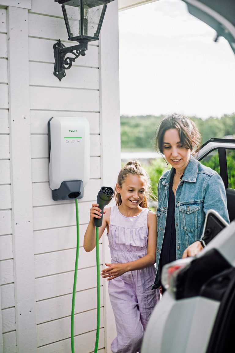 Mädchen hält Stecker des Ladekabel einer Wallbox von KEBA in der Hand und geht zum E-Auto.