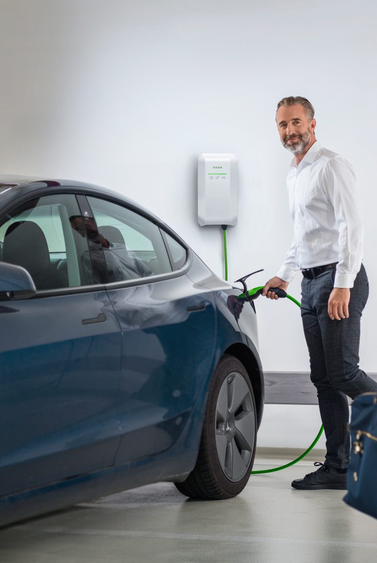 Mann steckt Ladekabel einer Wallbox von KEBA an sein E-Auto das in der Garage steht.