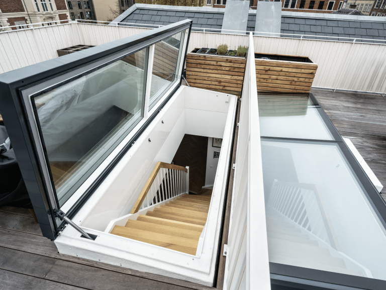 Lamilux zeigt einen Terrassenausstieg auf einer Dachterrasse durch ein großes Fenster und Wendeltreppen aus Holz mit weissem Geländer.