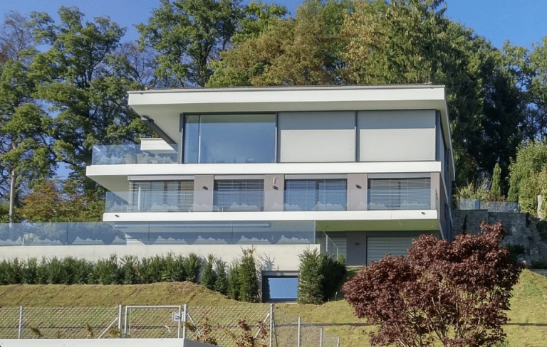 Architektenhaus in Hanglage mit mehreren Balkonen mit Glasgeländern und Fenstern von M SORA.