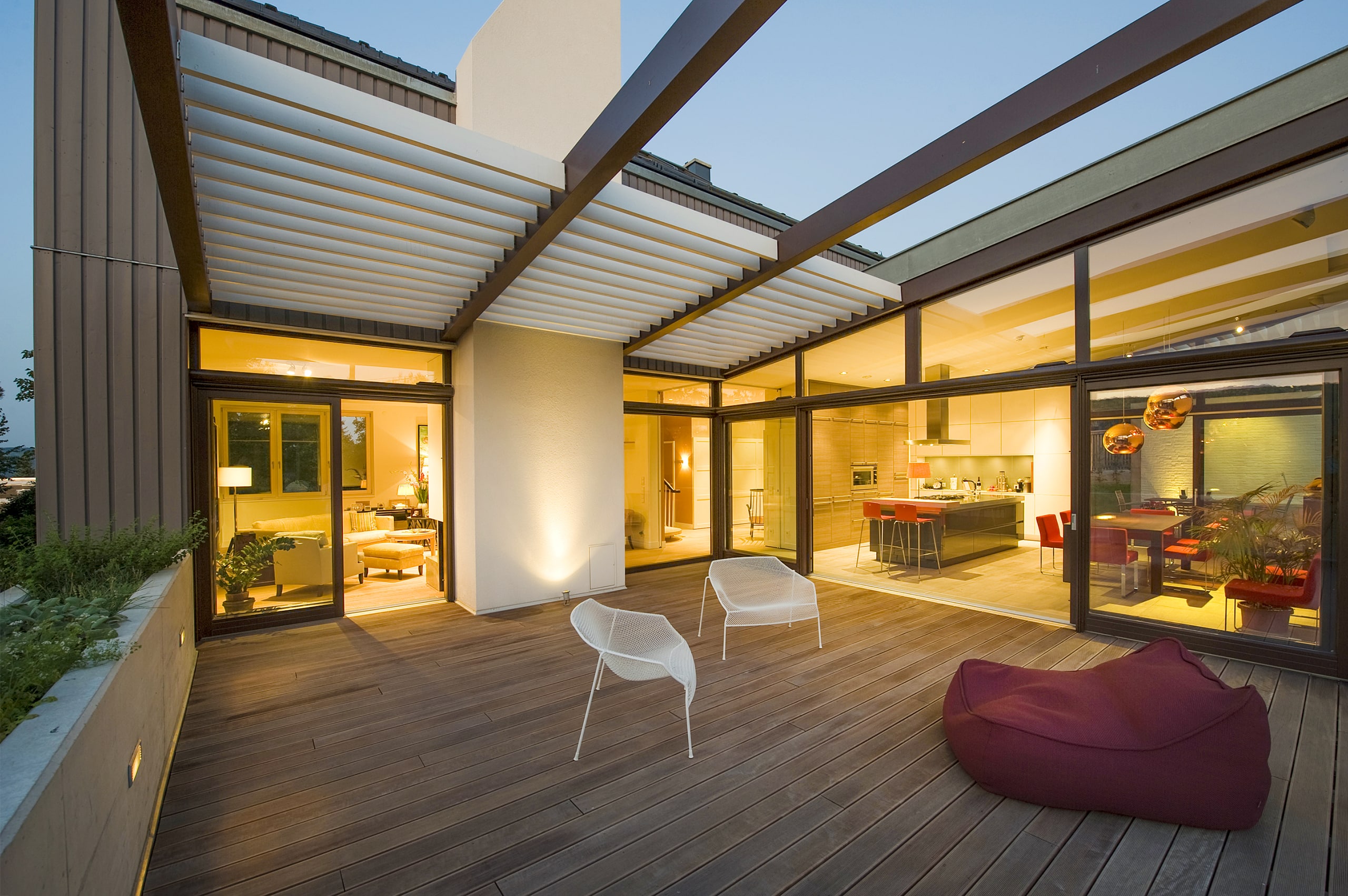 Maderböck Fenster und Türen präsentiert ein modernes Haus mit breiten Schiebefenstern und Verglasung und großer Terrasse mit einer Überdachung via Pergola mit weißen Lamellen.