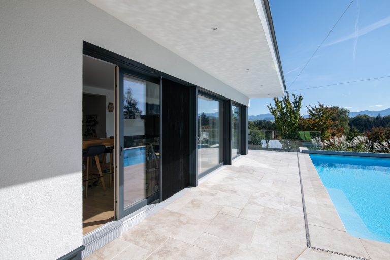 Die barrierefreien und bodentiefen Glasschiebetüren mit schwarzem Rahmen von Maderböck führen auf die Terrasse mit Pool.