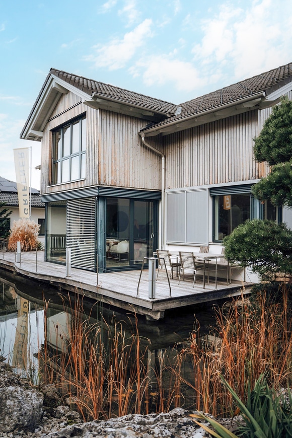 Einfamilienhaus mit Terrassenschiebetüren und einer Terrasse die als Holzsteg für den Teich dient im Musterhauspark Graz.