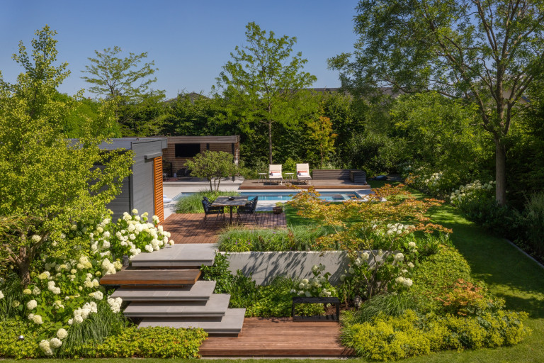 Praskac Pflanzenland Prachtgarten zeigt Bungalow mit schön bepflanztem Garten mit Bäumen und Sträuchern und Pool.