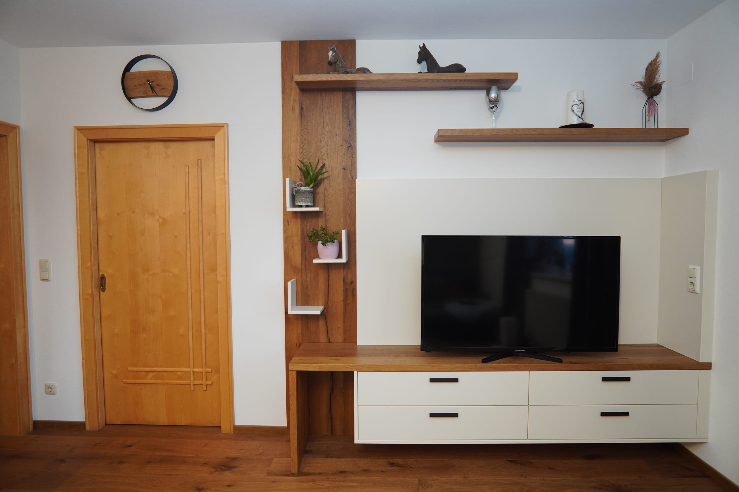 Wohnzimmer mit einer verspielten Medienwand mit Wandpaneelen und offenen schwebenden Regalen in einem Materialmix aus Holz und Beige von Pröll Wohnideen.