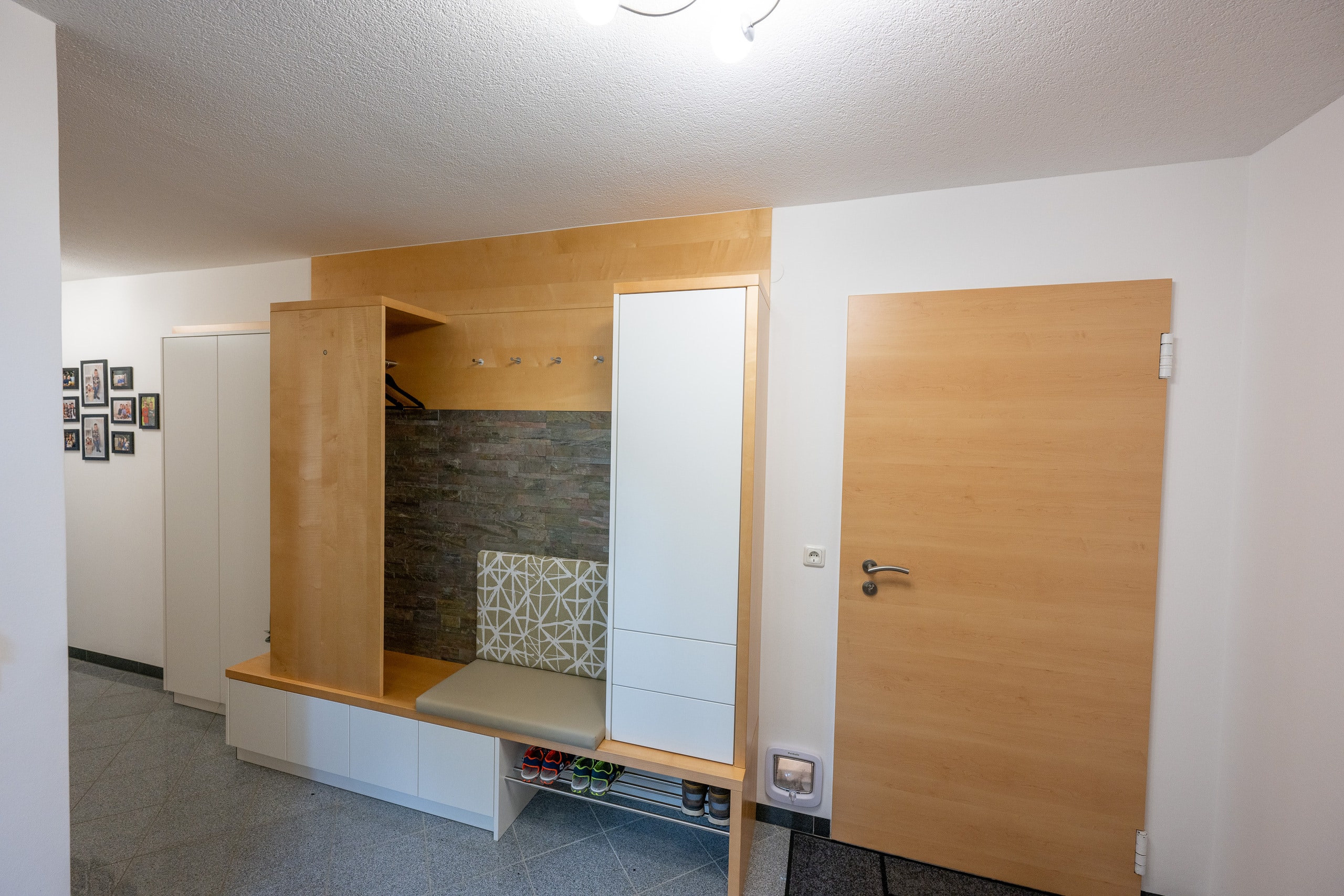 Garderobe und Vorzimmerverbau mit Sitzgelegenheit und Stauraum und Schuhablage in Weiß, Holz und Steinoptik von Pröll Wohnideen.