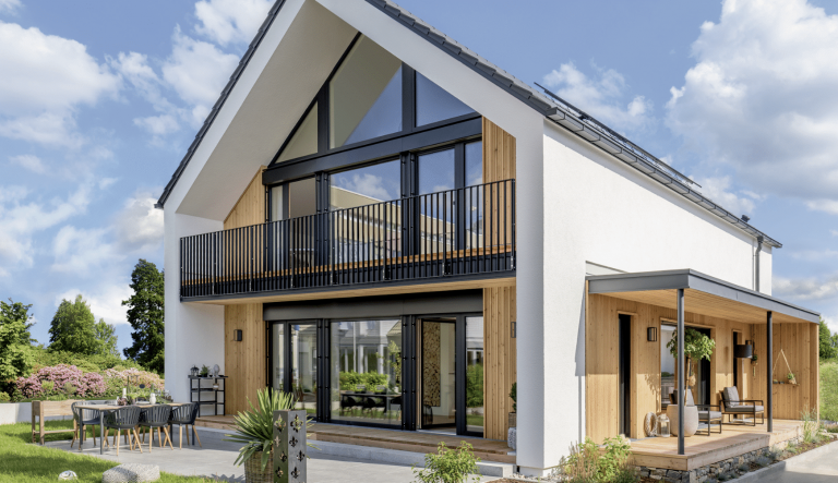 Regnauer zeigt ein modernes Einfamilienhaus mit Satteldach, Balkon mir dunklem Geländer, großer Terrasse und überdachtem Eingangsbereich.