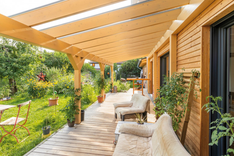 Regnauer Fertighaus zeigt überdachte Terrasse aus Holz mit Holzsäulen mit Blick in den Garten.