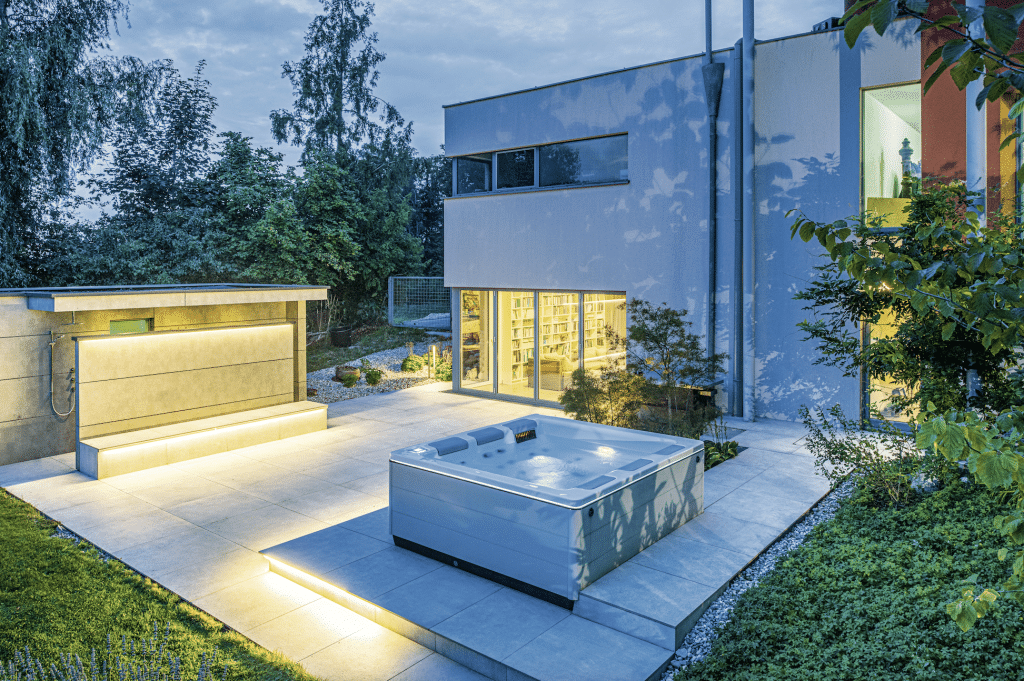 SAUNA-SCHWIMMBAD RUHA Stelzmüller zeigt eine Terrasse mit Saunahaus mit überdachter Außendusche und passendem Whirlpool.