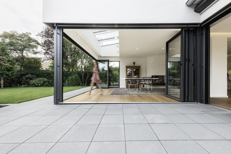 Solarlux zeigt helles Esszimmer mit Dachfenstern und zur Gänze geöffneten Faltschiebetüren mit dunkelgrauem Rahmen mit Blick auf den Garten.