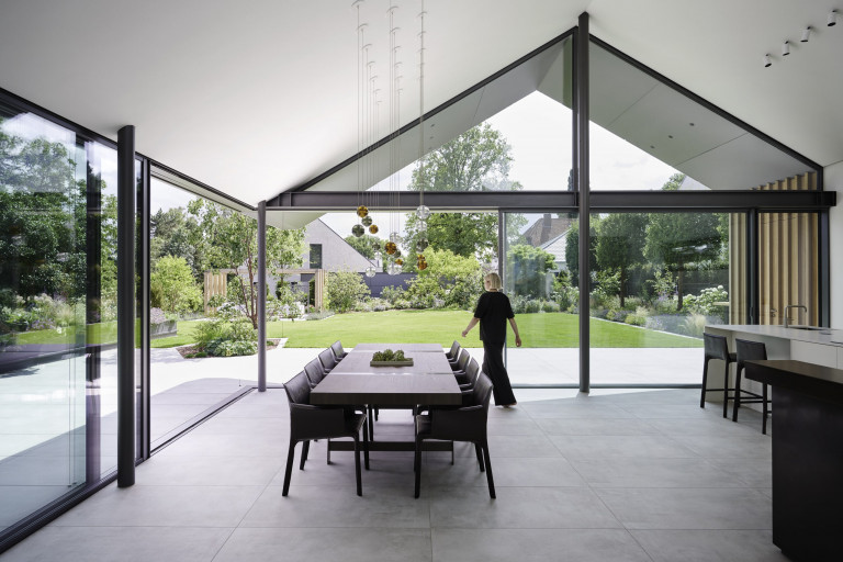 Moderner offener Wohnbereich mit Glasfronten in der Dachschräge und bodenbündigen Glasschiebetüren von Solarlux mit dunkelgrauem Rahmen mit Blick auf Terrasse und Garten.