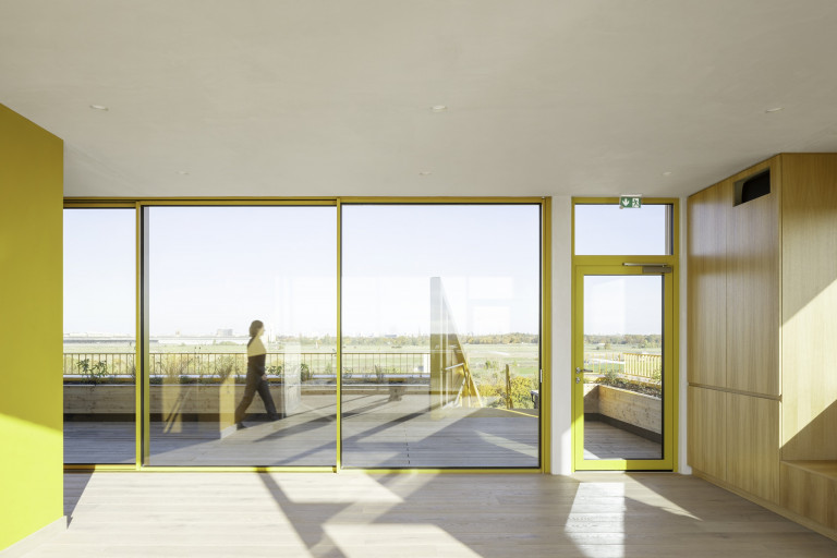 Solarlux zeigt bodenbündige Glasschiebetür mit gelbem Rahmen mit Blick auf die große Terrasse.