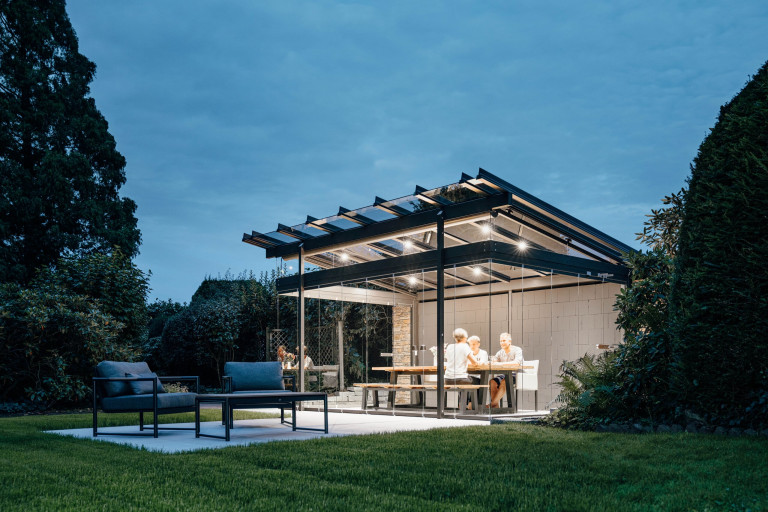 Modernes Gartenhaus mit Glas-Pultdach und Glasfaltwänden von Solarlux bei Abendstimmung.