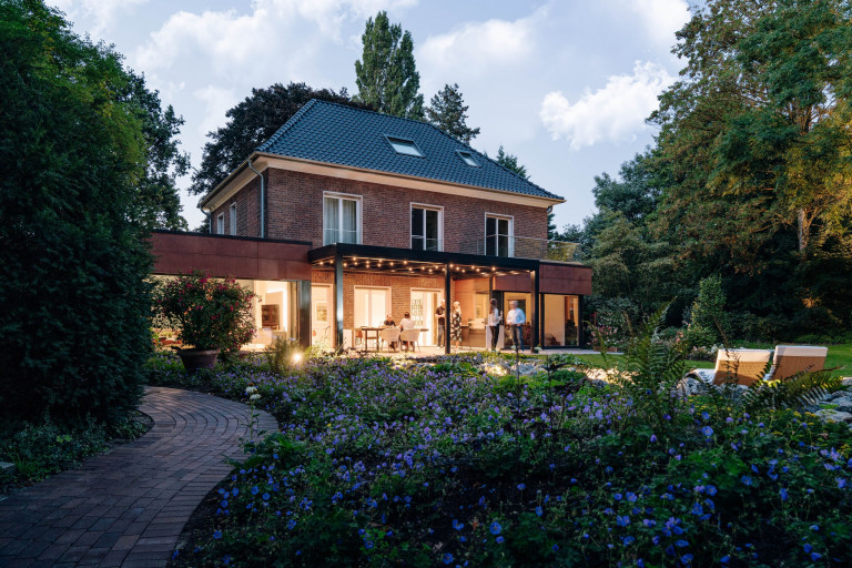 Solarlux zeigt überdachte Terrasse aus Alu und Glas in einem klassischen Landhaus bei Abendstimmung.