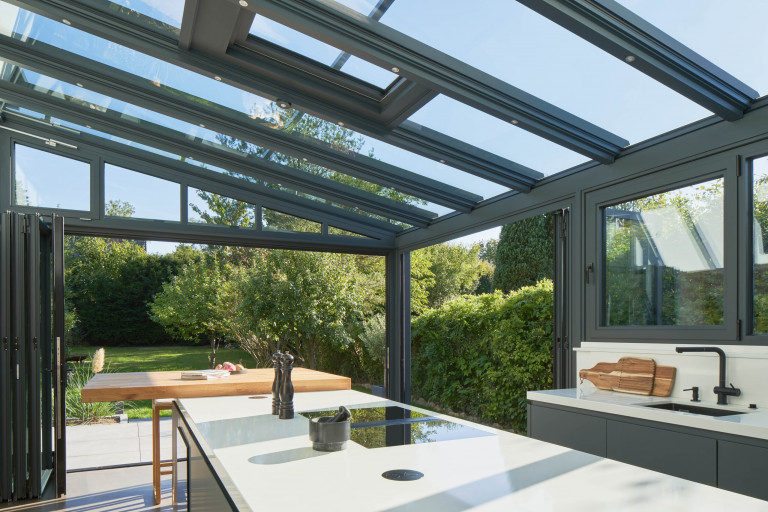 Solarlux zeigt modernen Küche im Wintergarten mit Glasfaltwänden mit Blick auf die Terrasse.