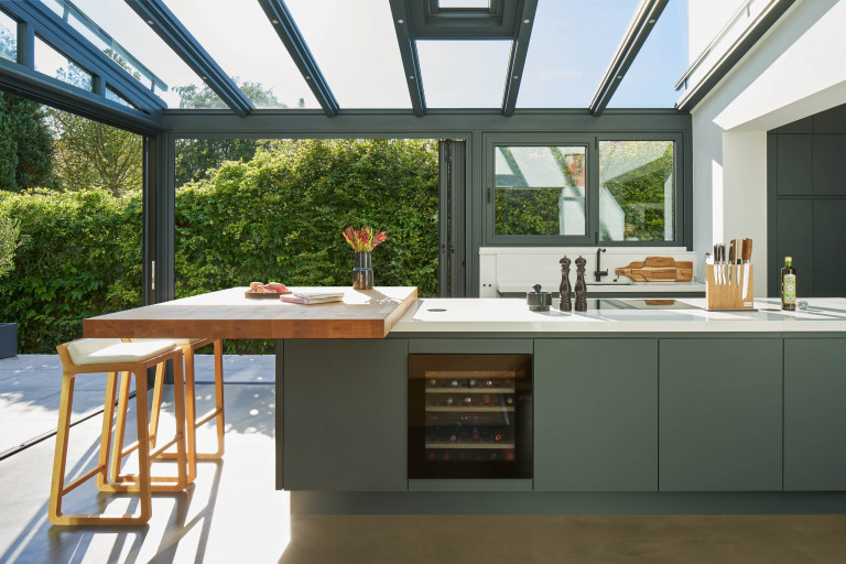 Solarlux zeigt moderne Küche im Wintergarten mit Glasfaltwänden mit Blick auf die Terrasse.