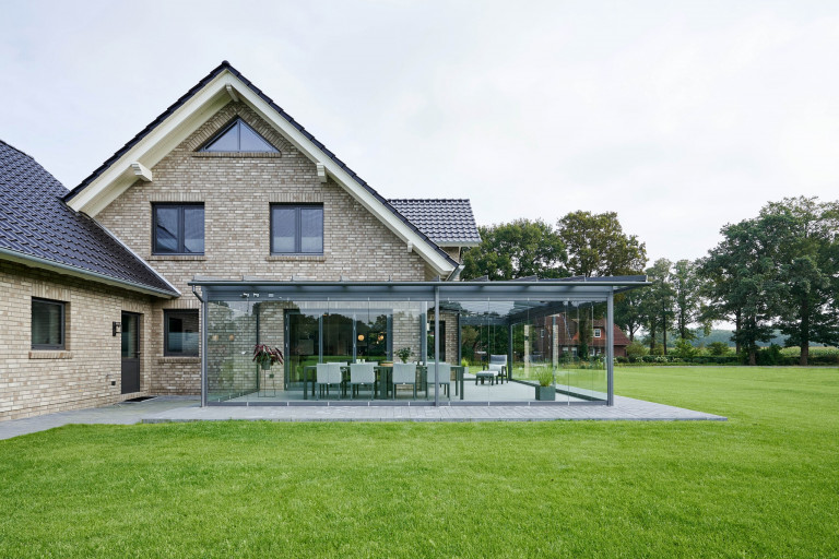 Modernes Backsteinhaus mit großem Wintergarten mit Glasfaltwänden von Solarlux mit Steinplatten und einem gepflegtem Rasen umrandet.