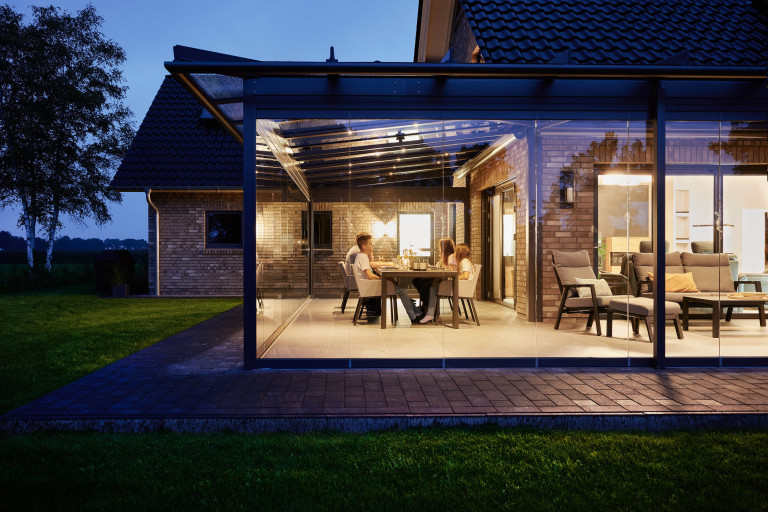 Modernes Backsteinhaus mit großem Wintergarten mit Glasfaltwänden von Solarlux mit Steinplatten umrandet bei Abendstimmung.