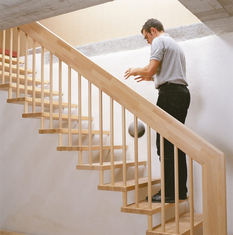 Ein Mann spielt auf einer Holztreppe mit Trittschallschutz von Treppenmeister mit einem Ball.