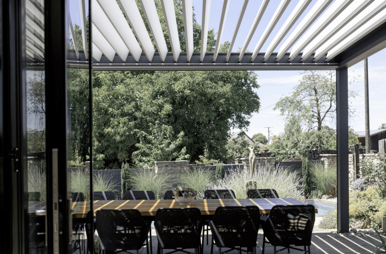 WAREMA präsentiert die überdachte Terrasse mit Lamellendach, einer großen Tischtafel im Garten eines Einfamilienhauses.