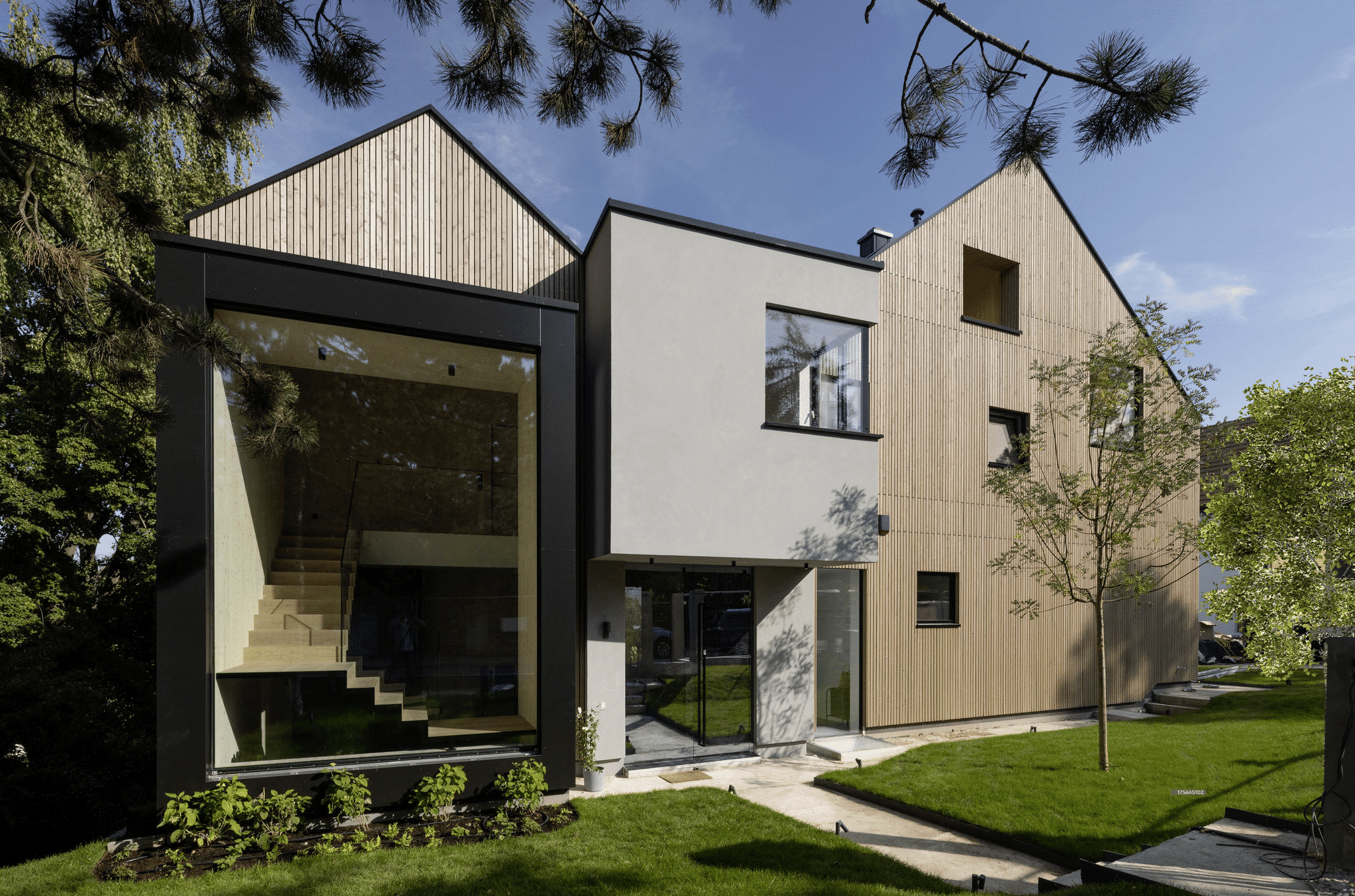 Weissenseer Holz-System-Bau zeigt modernes Wohnhaus mit Holzfassade, doppeltem Satteldach, Mittelbau mit Flachdach und grosser Glasfront mit Blick auf den Stiegenaufgang.