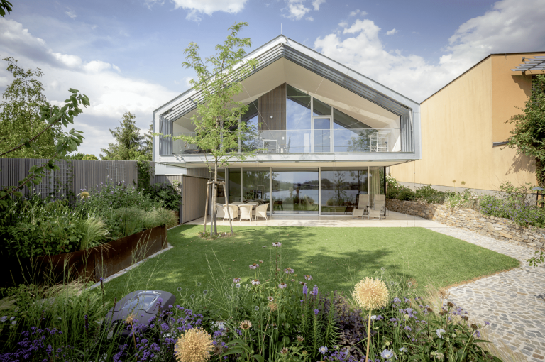 Villa mit Satteldach, überdachtem Balkon, Terrasse und Garten von Weissenseer Holz-System-Bau.