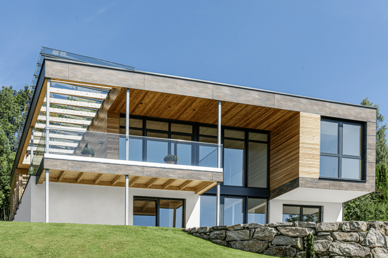 Einfamilienhaus mit Flachdach, Balkon, bodentiefen Fenstern und einer Holzfassade von Weissenseer Holz-System-Bau.