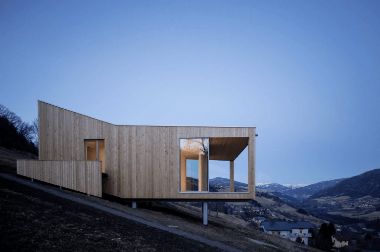 Modernes Einfamilienhaus in Hanglage mit Holzfassade, Balkon und Ganzglassystem von Weissenseer Holz-System-Bau.